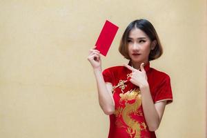 portret mooi Aziatisch vrouw in cheongsam jurk, thailand mensen, blij Chinese nieuw jaar concept, gelukkig Aziatisch dame in Chinese traditioneel jurk Holding een rood envelop foto