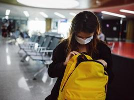 een passagier in een medisch masker Bij de luchthaven looks in een geel rugzak foto