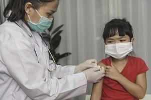 Aziatisch dokter injectie vaccin voor beschermen virus covid-19 naar een meisje slijtage medisch masker, mensen zijn meisjes zijn gevaccineerd tegen influenza elke jaar. foto