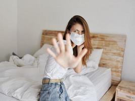 emotioneel vrouw gebaren met haar handen terwijl zittend Aan de bed medisch masker quarantaine isolatie foto