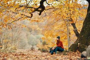 vrouw in herfst in de park in de buurt een groot boom en in een rugzak Aan de grond foto