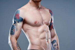 sexy atleet met naakt torso en gemotiveerd omhoog spieren tatoeëren grijs achtergrond model- foto