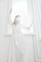 vrouw in wit jurk in de buurt venster poseren romance van de zon foto