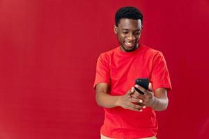 Mens van Afrikaanse uiterlijk in een rood t-shirt met een telefoon in zijn handen technologie bericht foto