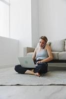 freelance vrouw met laptop en telefoon werken van huis zittend Aan de verdieping in haar huis kleren met een kort kapsel, vrij kopiëren ruimte foto