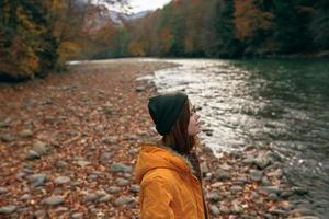 vrouw in herfst kleren Aan natuur in de buurt de rivier- wandelen de bergen foto