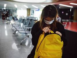 vrouw op zoek in geel rugzak luchthaven medisch masker aan het wachten foto