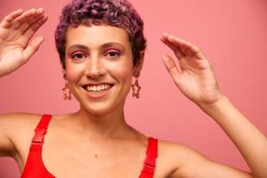 mode portret van een vrouw met een kort kapsel van Purper kleur en een glimlach met tanden in een rood top Aan een roze achtergrond geluk foto