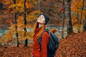 vrouw in een hoed met een rugzak en een trui is resting in de herfst Woud in de buurt de rivier- in natuur foto