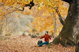 vrouw met een rugzak onder een boom in de park en vallend bladeren herfst landschap foto