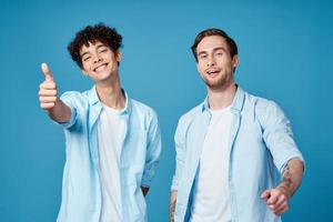 twee vrienden in identiek overhemden en een t-shirt gebaren met hun handen Aan een blauw achtergrond foto