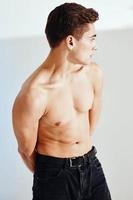sexy bodybuilder met gemotiveerd omhoog arm spieren looks terug en zwart broek grijs achtergrond foto