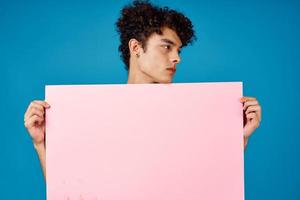 Mens met gekruld haar- Holding roze poster banier blauw achtergrond foto