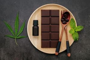 cannabisblad met donkere chocolade, plantenbladeren en houten keukengerei op een donkere betonnen achtergrond foto