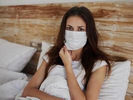 vrouw in medisch masker leugens in bed in quarantaine pandemisch coronavirus foto