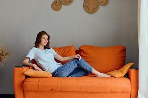 vrouw Aan de oranje bankstel in de rust uit kamer poseren levensstijl foto