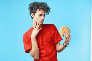 vent met gekruld haar- in rood t-shirt Hamburger snel voedsel blauw achtergrond foto