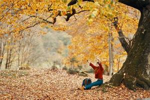 vrouw met een rugzak onder een boom in de park en vallend bladeren herfst landschap foto