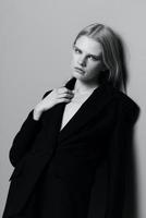 portret van een mooi blond in een klassiek jasje leunend tegen de muur in de studio. zwart en wit stijl. concept voor kleding merken foto