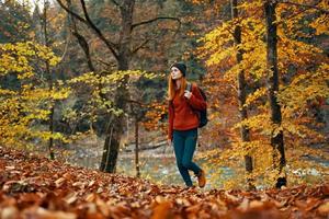 vrouw toerist wandelingen door de park in herfst met een rugzak Aan haar terug en hoog bomen landschap rivier- meer foto