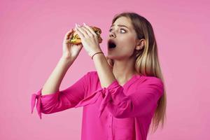 vrolijk blond in een roze overhemd Hamburger snel voedsel tussendoortje foto