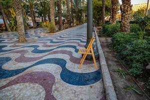 uitleg promenade in Alicante Spanje mijlpaal met houten leeg stoel Aan mozaïek- foto