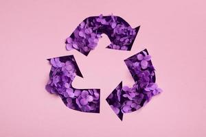 Purper bloemen onder papier besnoeiing recycling symbool. opslaan planeet recycling kleding concept, circulaire mode. foto