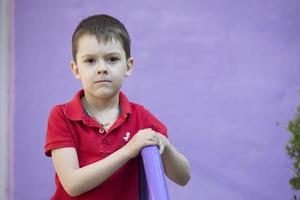 zes jaar oud jongen. primair school- leerling. kleuter. kind Aan een Purper achtergrond. bruine ogen jongen in een rood t-shirt. foto