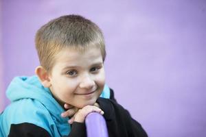 zes jaar oud jongen. primair school- leerling. kleuter. kind Aan een Purper achtergrond. weinig blond jongen glimlacht. foto