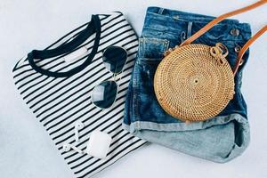 voorjaar en zomer vrouwen kleding en accessoires. gestreept t-shirt, blauw denim shorts en modieus biologisch rotan tas. vlak leggen foto, top visie foto