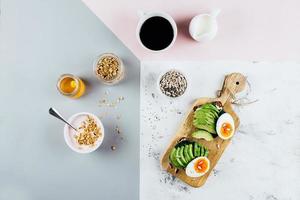 gezond ontbijt concept. belegd broodje met avocado en gekookt eieren, yoghurt met muesli, kop van koffie over- driekleur elegant achtergrond, top visie, kopiëren ruimte, vlak leggen foto