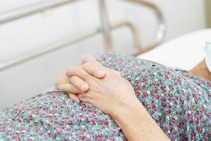 Aziatische oudere oudere vrouw die bedhek vasthoudt terwijl ze met hoop ligt te wachten op haar familie in het ziekenhuis. foto