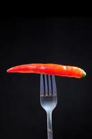 rode chili peper op een vork op zwarte achtergrond foto