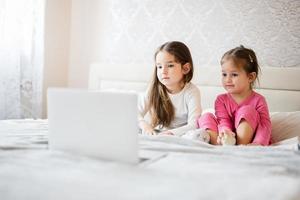 twee schattig weinig zussen slijtage pyjama op zoek tekenfilm door laptop in ochtend- Bij huis. foto