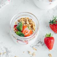 ontbijt voedsel concept. pot met smakelijk parfaits gemaakt van muesli, aardbeien en yoghurt Aan marmeren tafel foto