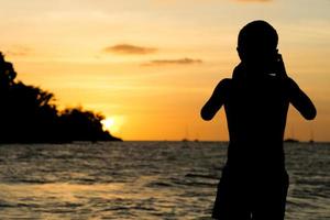 silhouetportret van jonge jongen die een zeegezichtscène op het strand met licht van zonsondergang nemen foto