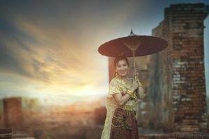 mooi Aziatisch vrouw Holding bamboe paraplu staand tegen oud tempel in ayutthaya wereld erfgoed plaats van UNESCO Thailand foto