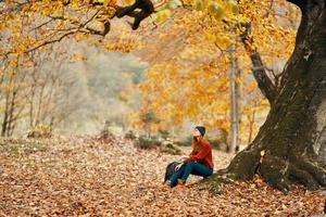 vrouw in herfst in de park in de buurt een groot boom en in een rugzak Aan de grond foto