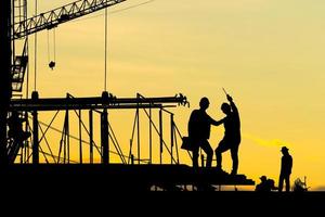 silhouet van ingenieur en werknemer die project controleren op de achtergrond van de bouwplaats, bouwplaats bij zonsondergang in de avondtijd foto
