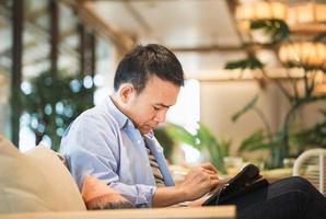 Mens tekening een grafiek Aan tablet in een modern koffie winkel, Aziatisch Mens gebruik makend van een tablet, technologie in gebruik concepten foto