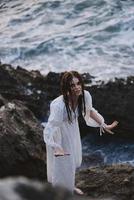 een vrouw in een wit jurk staat Aan de stenen door de oceaan natuur reizen foto