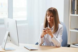 echt aanbiddelijk blond zakenvrouw arbeider freelancer kijken Bij telefoon typen bericht in licht modern kantoor. werknemer werk aan het doen Uitmaken chatten met bedrijf partner lezen nieuws. kopiëren ruimte foto