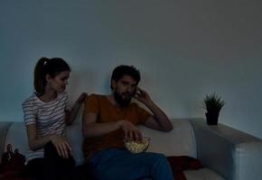 emotioneel vrouw en Mens met een bord van popcorn aan het kijken TV in de avond binnenshuis foto