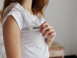 vrouw cheques temperatuur met thermometer oksel slaapkamer foto