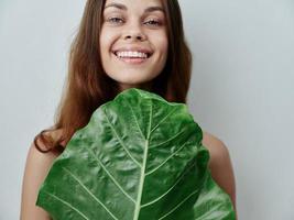 glimlachen vrouw en flatteert een groen blad in voorkant van haar naakt schouders exotisch foto