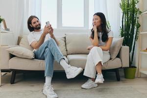 een Mens looks Bij zijn telefoon scherm en glimlacht gedurende een argument met zijn vriendin. de boos en pijn doen vrouw looks in zijn richting en is verdrietig. familie onenigheid Bij huis, telefoon verslaving foto