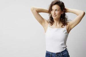 gelukkig vrolijk nadenkend gekruld mooi vrouw in eenvoudig wit t-shirt accenten haar- looks terzijde poseren geïsoleerd Aan over- wit achtergrond. mensen emoties levensstijl concept. kopiëren ruimte foto