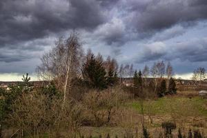 herfst landschap met bladerloos bomen en donker wolken in de lucht en een oud gebouw foto