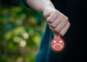 vrouw hand- Holding verdrietig gezicht icoon Aan natuur achtergrond. negatief emotie concept. klant onderhoud evaluatie concept. foto