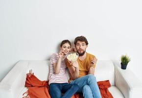 geïnteresseerd Mens en vrouw met popcorn Aan sofa oranje plaid en bloem in een pot foto